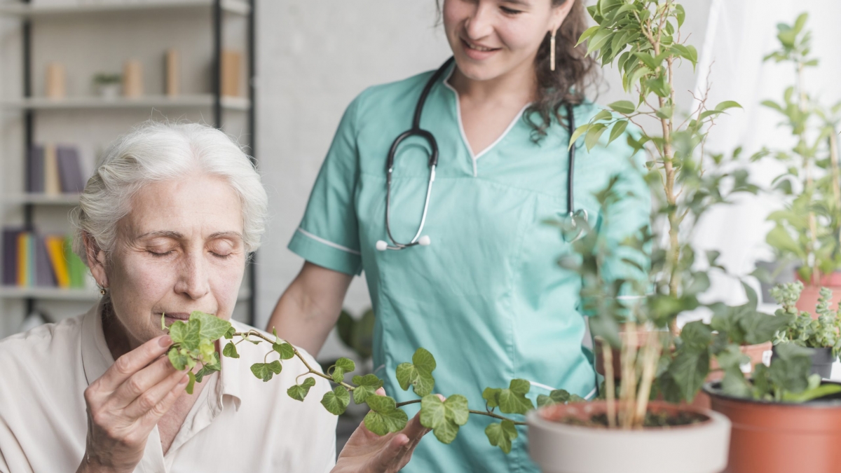 nurse-looking-at-senior-female-patient-smelling-ivy-plant-in-the-pot