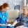 Female doctor taking blood pressure of senior woman in nursing home sitting on sofa