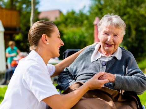 Nurse holding hands with senior woman sitting in wheelchair in garden of retirement home